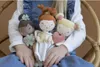 A child is holding three plush dolls in their lap. Náhled obrázku produktu