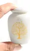 A hand holding a small white urn with a gold tree design. Náhled obrázku produktu