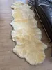 A sheepskin rug is laid out on a wooden floor next to a dark leather sofa. Produktbild-Vorschau
