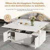 A white coffee table with its top extended and open storage compartments, shown in a living room setting with a sofa in the background. Produktbild-Vorschau