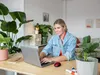 A woman is working on a laptop at a desk with plants around her. Anteprima dell’immagine prodotto
