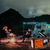 Two people are sitting in camping chairs around a campfire at night, with a van and tent in the background. An emergency radio is in the foreground. Náhled obrázku produktu