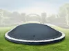 A dark gray inflatable pool cover is shown on a green lawn in a garden setting with blurred trees and arches in the background. Produktbild-Vorschau