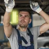 A mechanic working on a car, illuminated by a work light. Voir les images du produit