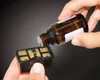 A hand is pouring liquid from a small brown bottle into a black filter component. Produktbild-Vorschau