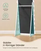 The back view of a full-length mirror with a white frame, standing on a wooden floor against a light beige wall. The mirror has a teal-colored, wavy design on its support legs, and there are informational icons and text overlays on the left side. Produktbild-Vorschau