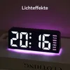 A digital alarm clock with a purple light effect is displayed on a surface. Produktbild-Vorschau