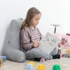 A young girl is sitting on a rug, leaning against a large gray pillow, and reading a book. There are building blocks and a pink toy car in the background. Voir les images du produit