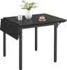 A black drop-leaf dining table with a vase of flowers, a mug, and a small cake on it. Produktbild-Vorschau