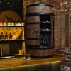 A wooden barrel-shaped cabinet with shelves and bottles displayed on a wooden counter in front of a brick wall. Náhled obrázku produktu