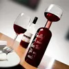A wine bottle that doubles as a wine glass, with a traditional wine glass and a bottle of white wine in the background, set on a wooden table. Náhľad obrázku produktu