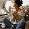 A woman is sitting in a chair, holding a mug and listening to music from a small speaker. Produktbild-Vorschau