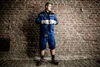 A man in workwear stands against a brick wall. Voir les images du produit