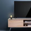 A black cage lamp with a visible bulb sits on a wooden TV stand next to a large black television. Produktbild-Vorschau