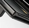 A close-up view of the corner of a black appliance, possibly a oven or grill, showing the textured metal frame and a glass surface. Produktbild-Vorschau