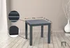 A dark gray square side table with dimensions indicated by arrows and text, placed on a wooden floor in a room with a light gray wall and a white vase with branches. Anteprima dell’immagine prodotto
