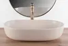 A beige matte washbasin with a gold faucet is placed on a wooden surface in front of a mirror. Podgląd zdjęcia produktu