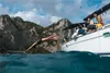 A woman dives into the ocean from a sailboat near a rocky coastline. Podgląd zdjęcia produktu