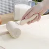 A hand is using a wooden rolling pin to flatten dough on a wooden surface. In the background, there is a jar of flour and some eggs. Anteprima dell’immagine prodotto