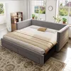 A gray upholstered daybed with storage drawers is shown in a room with windows and plants. Produktbild-Vorschau