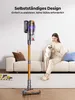 A woman is sitting on a couch holding a cat, with a cordless vacuum cleaner standing upright on the floor next to her. Toys are visible on the floor in the foreground. Produktbild-Vorschau
