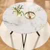 A round dining table with a marble-like top and black metal legs, set on a cream rug on a wooden floor. A vase of flowers and a decorative tray with candles and a drink are on the table. Produktbild-Vorschau