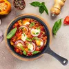 A close-up overhead view of a skillet filled with a colorful dish, likely shakshuka, with ingredients like eggs, tomatoes, onions, and basil, surrounded by other ingredients and a pepper grinder. Anteprima dell’immagine prodotto
