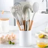 A set of kitchen utensils in a white holder on a countertop, with eggs and a lemon in the foreground. Produktbild-Vorschau