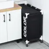 A black laundry basket with white text is placed next to a white cabinet in a bathroom. Náhled obrázku produktu