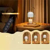 A candle warmer lamp with a remote control and a candle, presented in a bedroom setting with curtains and a bedside table. The bottom part of the image shows three smaller, stylized views of the lamp. Náhled obrázku produktu