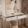 A white high-gloss console table with gold legs, featuring open drawers and decorative items on top, set against a neutral background with curtains. Produktbild-Vorschau