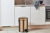 A copper pedal bin is placed on a tiled floor in a modern kitchen, next to white cabinets and a countertop with a sink and a dish towel. Anteprima dell’immagine prodotto