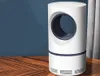A white cylindrical insect repellent lamp with a dark blue accent band and a circular opening on a wooden table against a blue wall. Produktbild-Vorschau