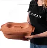 A person is holding a terracotta oval baking dish with a lid. Voir les images du produit