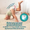 A baby is doing a handstand on a fluffy carpet, wearing a diaper. There is marketing text and a diagram of the diaper's features. Podgląd zdjęcia produktu