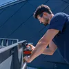 A man is using a cordless drill to work on a metal railing outdoors. Voir les images du produit