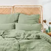 A close-up view of a bed with green musselin bedding and a woven headboard. Produktbild-Vorschau