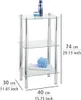 A three-tiered glass shelf unit with chrome legs, holding a bottle of shampoo, a small bowl, a folded towel, and a blue bath pouf. Produktbild-Vorschau