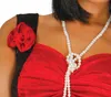 Close-up of a person wearing a red dress with black straps and a pearl necklace. Produktbild-Vorschau