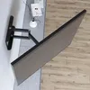 A wall mount for a flat-screen television is shown attached to a wall, with the television itself angled away from the wall. Decorative items like a vase and books are visible on a rug next to the mount. Anteprima dell’immagine prodotto