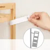 A hand is shown attaching a white strap to a wooden shelf unit with a screw, demonstrating how to secure it to a wall. An inset diagram shows the shelf unit leaning against a wall, secured by a strap. Produktbild-Vorschau