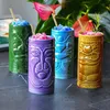 Four tiki mugs filled with colorful slushy drinks and straws, set against a backdrop of tropical plants and flowers. Podgląd zdjęcia produktu