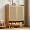 A wooden shoe cabinet with rattan doors and shelves, displaying shoes and decorative items on top. Produktbild-Vorschau