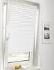 A white pleated blind is installed on a tilted window, partially covering the view outside. Two framed pictures hang on the wall to the right of the window, and a small bowl with fruit sits on the windowsill below. Produktbild-Vorschau