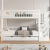 A white bunk bed with a pull-out trundle bed and stairs with drawers, set up in a bedroom. Náhled obrázku produktu