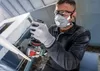 A person wearing safety gear is using a power tool to cut a piece of drywall. Voir les images du produit
