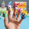 A hand with five fingers, each adorned with a colorful clay monster finger puppet. The background shows more clay creations and a blurred wooden frame. Náhled obrázku produktu