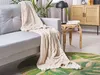 A beige blanket draped over a light gray sofa in a living room setting. Náhled obrázku produktu