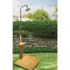An outdoor shower set up in a garden with a stone wall and greenery in the background. Voir les images du produit