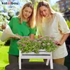 Two young women are gardening together in a sunny outdoor setting, tending to a white wooden planter box filled with pink flowers. Produktbild-Vorschau
